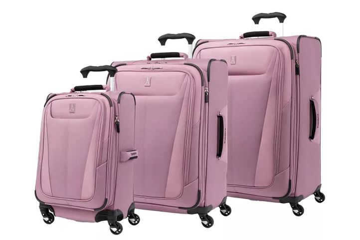 five softside suitcases lined up against a wall, mixed brands and colors